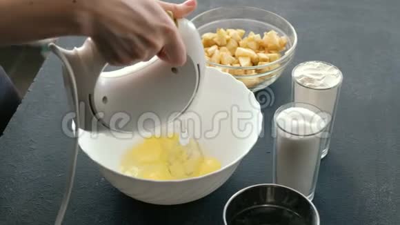 特写女人用搅拌器她的手在碗里搅拌鸡蛋并加入糖做苹果派视频的预览图