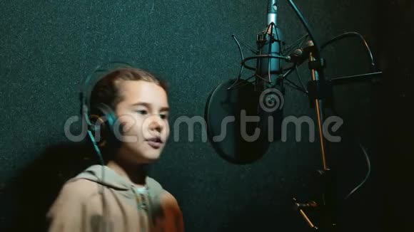 在专业录音室用耳机录制歌曲的年轻女孩小女孩在唱一首歌视频的预览图