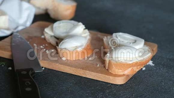 妇女用手腌制的三明治面包黄油和鸡蛋放在黑色背景的木板上做三明治视频的预览图