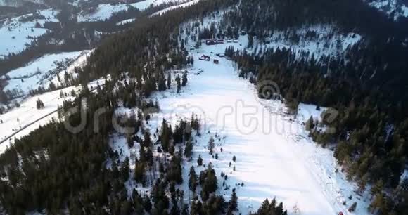 空气视图飞越冰冷的松林向冬季度假胜地和滑雪坡飞去滑雪跑道冬季太阳升起视频的预览图