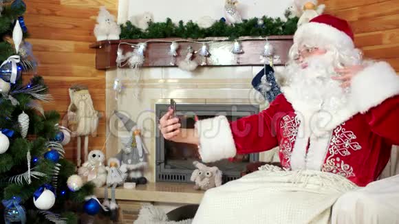 圣诞老人用智能手机自拍用电子设备室内壁炉做鬼脸视频的预览图
