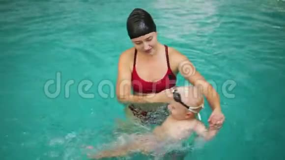 年轻的母亲教她的小男孩如何在游泳池里游泳宝宝用脚在水里踢开始视频的预览图