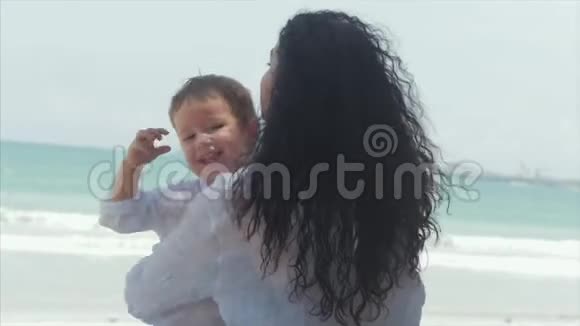 快乐的母亲在海岸拥抱她的孩子可爱的孩子亲吻他的妈妈轻轻拥抱儿童户外运动概念妈妈视频的预览图