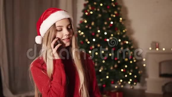 快乐的年轻女人在圣诞树附近说手机视频的预览图