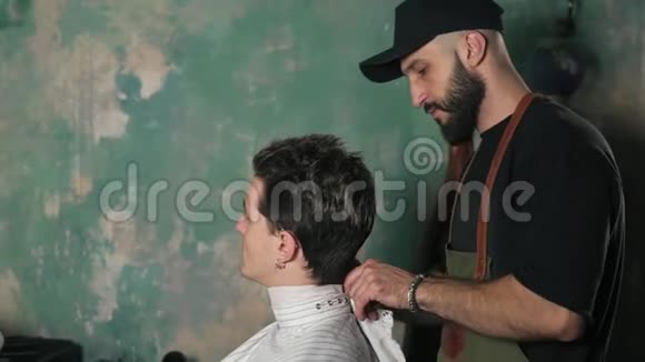 漂亮的年轻人坐在椅子上而胡子理发师正在为他理发时尚理发店视频的预览图