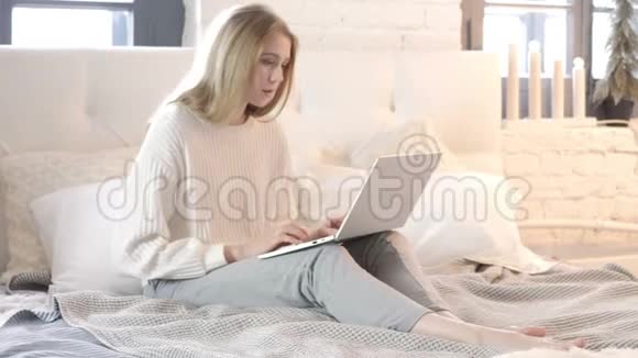 坐在床上打字的年轻女子视频的预览图