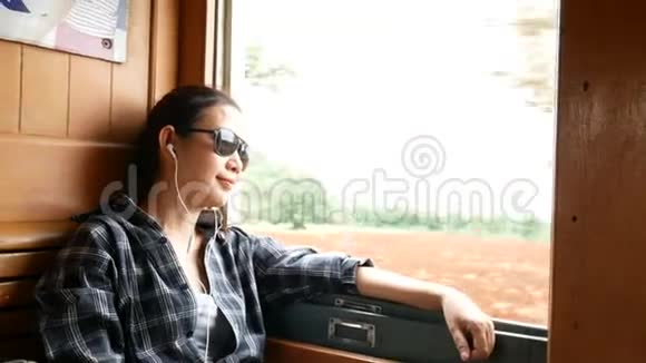 4K美丽的亚洲女人戴着太阳镜听着耳机里的音乐看着火车窗口享受交通视频的预览图