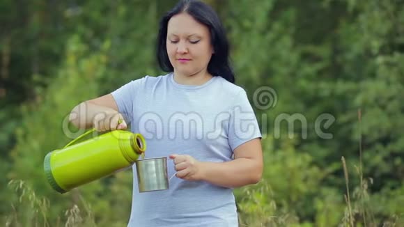 一个在森林里旅行的女人把热水瓶里的热茶倒进杯子里视频的预览图