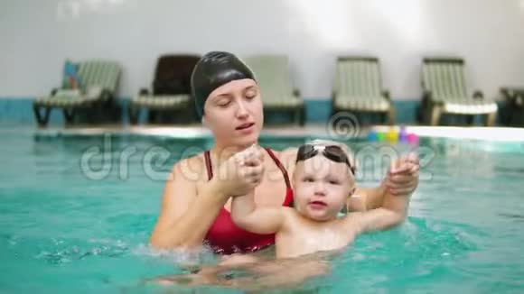 慢镜头的快乐微笑的小孩子和他的母亲一起在游泳池游泳年轻的母亲视频的预览图
