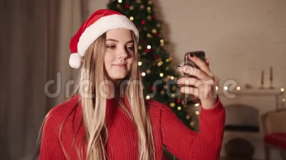 快乐的年轻女人在圣诞树附近说手机视频的预览图