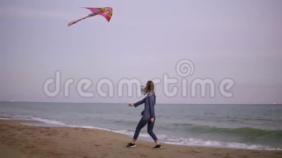 快乐的年轻女子留着长发傍晚在沙滩上放着五颜六色的风筝伴着它奔跑视频的预览图