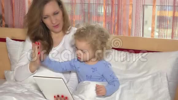 妈妈和可爱的女儿躺在家里的床上看着数码平板电脑视频的预览图