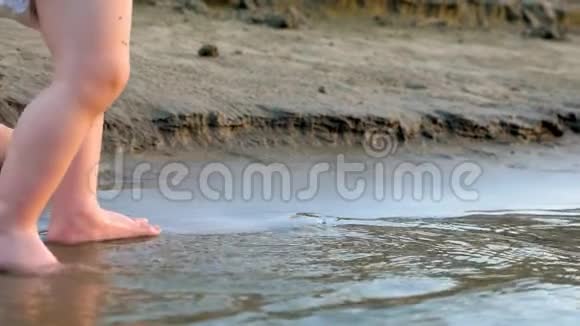 婴儿穿着尿布沿着河岸走第一步洒上水和母亲一起散步腿特写视频的预览图