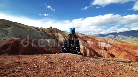年轻的女游客坐在红山的边缘背景中有风景和多云的天空视频的预览图