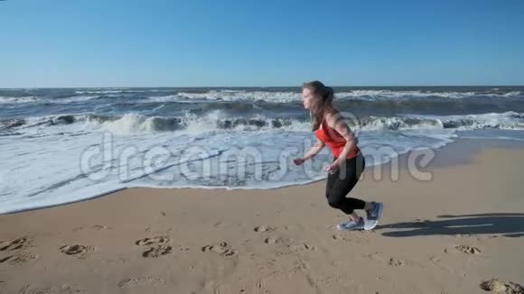 肖像一个年轻女孩穿着红色运动服沿着海滩奔跑听耳机上的音乐晚上表演或者视频的预览图