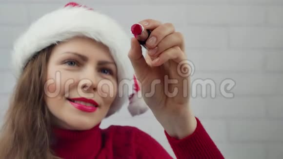祝2018年新年快乐圣诞老人女孩用口红在2018年的玻璃单词上写字戴着圣诞帽的漂亮女孩在发信息视频的预览图