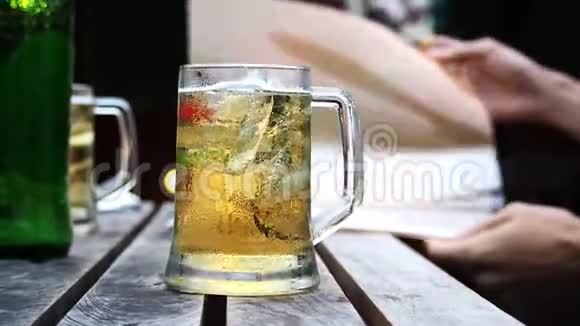 啤酒在玻璃木桌上和手打开食品菜单背景模糊杯子里的啤酒放在木桌上用手打开视频的预览图