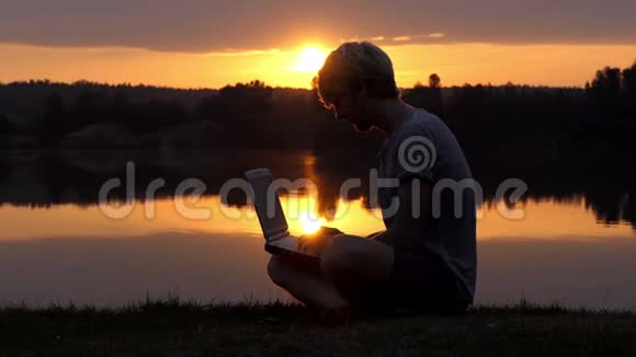 在夕阳西下的河岸上他的笔记本电脑上的创意万种视频的预览图