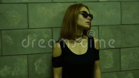 一位戴着眼镜穿着黑色T恤的孤独女士站在行人通道的墙边视频的预览图