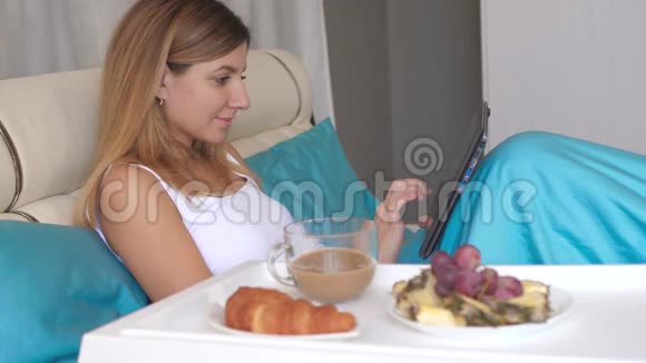 年轻女子在家里的床上吃早餐喝咖啡视频的预览图