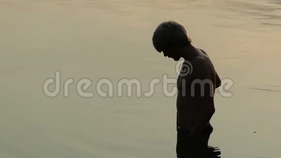 人站在河水里他的手指在日落的海面上行走视频的预览图