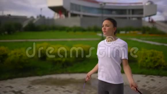 年轻女子在摩天轮的背景下在公园里跳绳慢动作视频的预览图