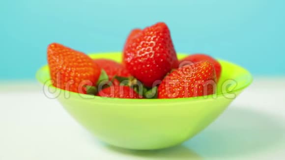 成熟的多汁草莓在绿色的盘子在蓝色的背景旋转成一个圆圈视频的预览图
