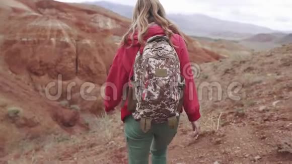 女孩旅行者带着背包在山区行走后景红色的山脉和红色的地球就像火星一样视频的预览图