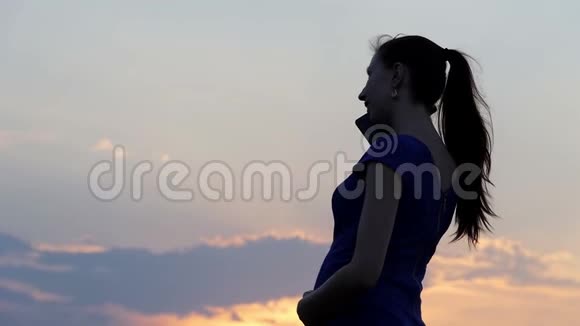 一个快乐的孕妇在太阳落山时打电话给她的朋友视频的预览图