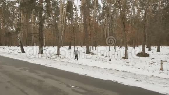 年轻的蓄胡子运动员沿着靠近森林的冬季道路奔跑视频的预览图