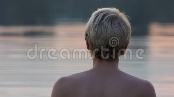 年轻男子站在湖水中在斯隆莫的灿烂的日落中从后面射出视频的预览图