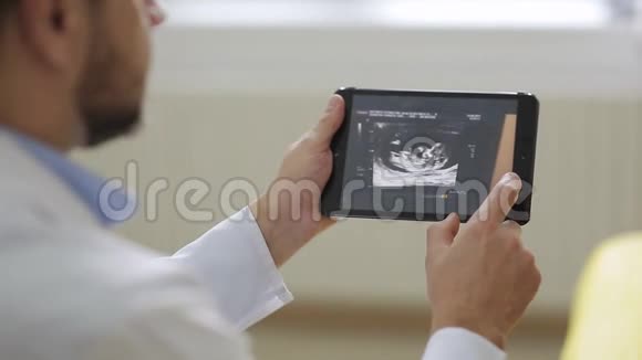 穿着白色长袍的医生在平板电脑上向孕妇展示超声波照片视频的预览图