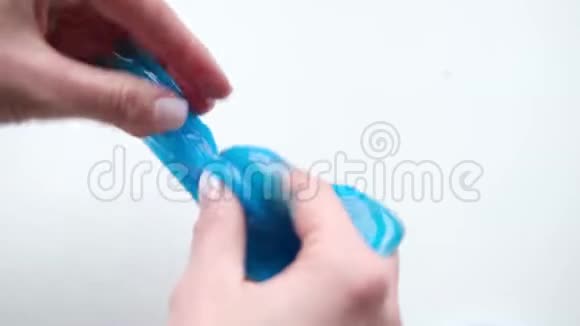 女孩把蓝色的黏液伸到两边女人的手在玩黏液玩具在白色上做黏液时髦的液体玩具棒视频的预览图