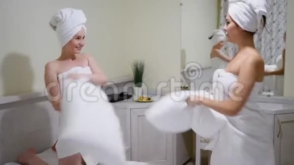快乐的女孩快乐的朋友在浴巾里玩得开心在卧室的床上用枕头互相拍打视频的预览图