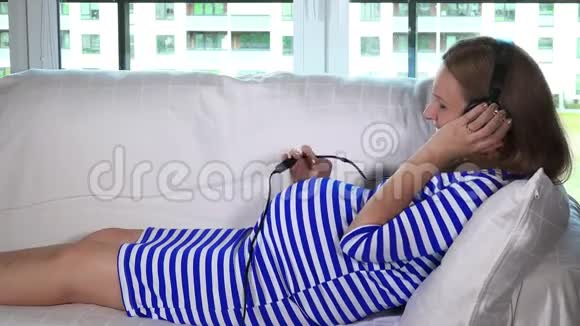 孕妇躺在沙发上戴着耳机听音乐视频的预览图
