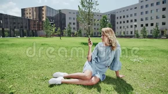 穿着蓝色牛仔裤的现代年轻女子绿色草地带着智能手机视频的预览图