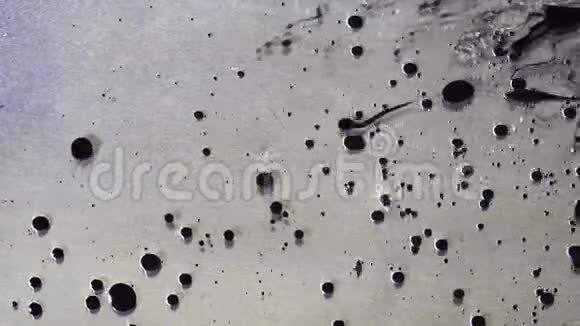 黑色墨水滴在金属灰色背景上的液体油中流动的顶部视图黑色的油漆球漂浮在视频的预览图