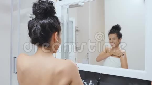 美丽的女人在镜子前用奶油滋润她的身体视频的预览图