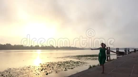 喜孕妇在夕阳下穿着绿色的衣服在河岸上奔跑视频的预览图