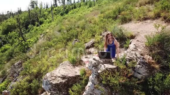 女孩用笔记本电脑在山上鸟瞰自然视频的预览图