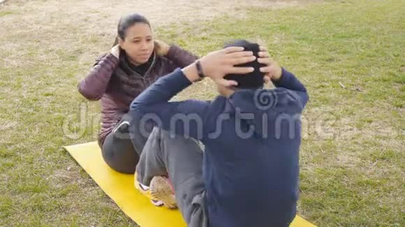 户外锻炼在秋天的雨天公园里拉丁美洲的年轻夫妇一起坐在普通的黄色垫子上视频的预览图