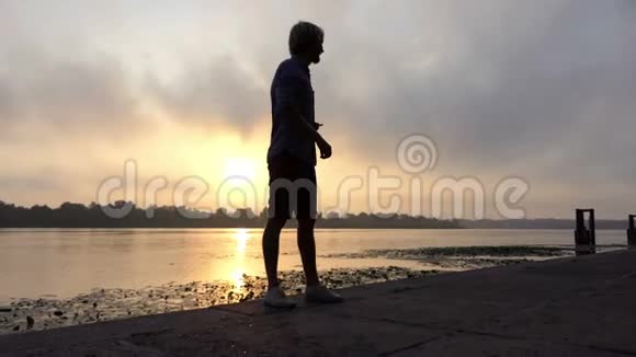 运动员在河岸上快乐地转过来日落时芦苇在缓慢地运动视频的预览图