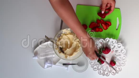 一个女人正在切草莓来装饰蛋糕附近是一个容器里的奶油视频的预览图