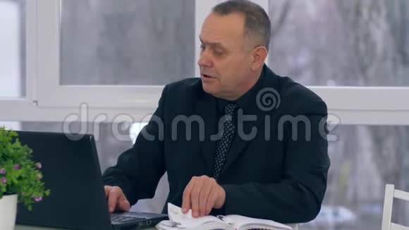 年长的商人在笔记本电脑上工作在办公室里记笔记视频的预览图