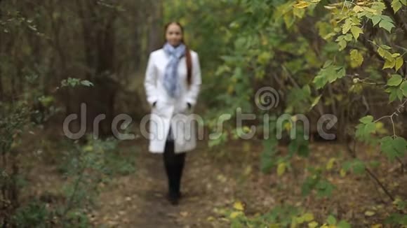 金发白种人中年妇女穿着白大褂在秋天公园的阴天散步视频的预览图