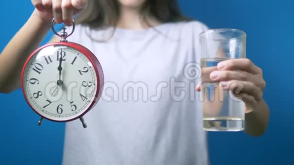 饮食观念那个女孩拿着闹钟和一杯水喝水的时间视频的预览图