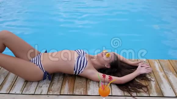 夏天穿泳衣的女孩躺在泳池边的露台上视频的预览图