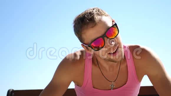 穿着粉色T恤戴太阳镜的帅哥看着相机突然指着相机视频的预览图