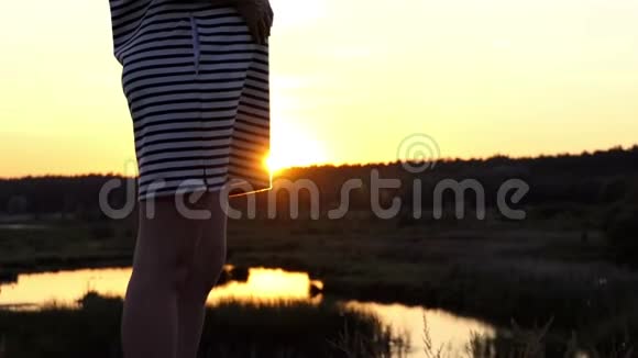 日落时分身穿条纹连衣裙的孕妇站在湖边视频的预览图
