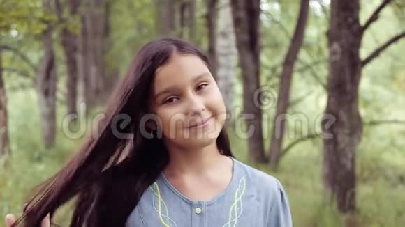 肖像一个甜美美丽的小女孩在摆姿势和摆弄头发时对着镜头笑得非常漂亮视频的预览图